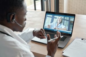 Black male doctor consulting senior patient by telemedicine online video call.