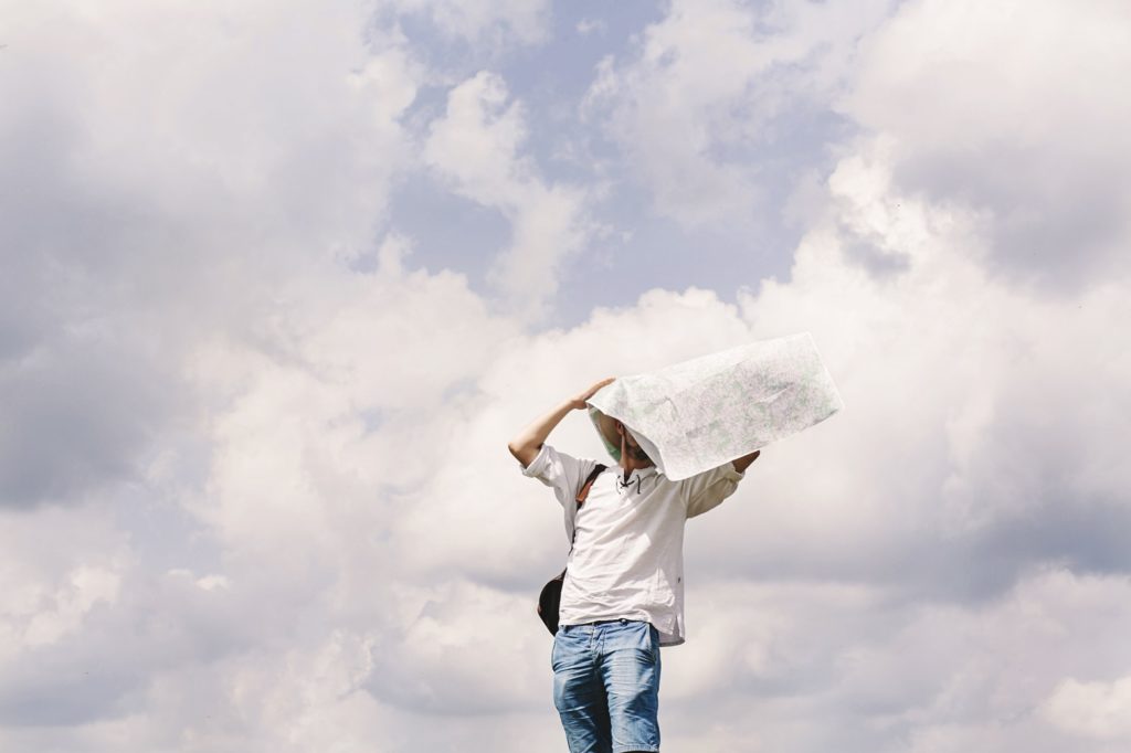 Hipster traveler on top of mountains with amazing sky clouds view and map at his head